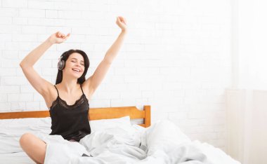 Kaygısız kadın müzik dinliyor, yatakta dans ediyor.