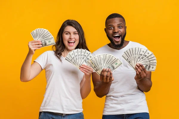 Joyful multiracial couple holding lot of dollar banknotes, rejoicing success together — Stock Photo, Image