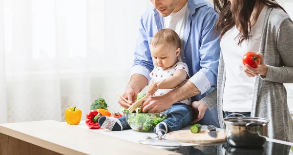 Entzückendes Baby kocht Gemüsesalat mit Eltern in der Küche — Stockfoto
