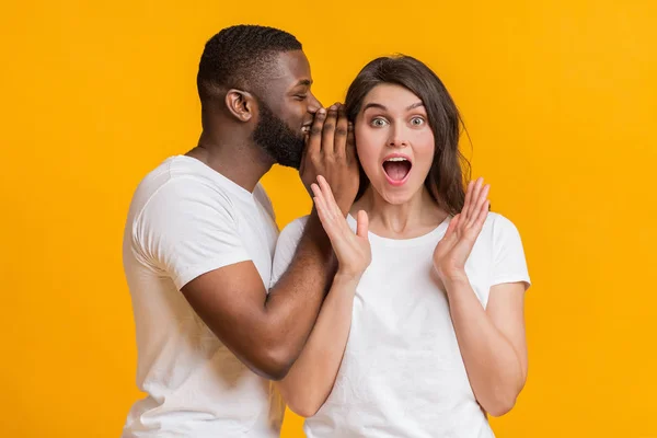 Usmívající se černoch šeptá něco do svého šokovaného přítelkyně ucho — Stock fotografie