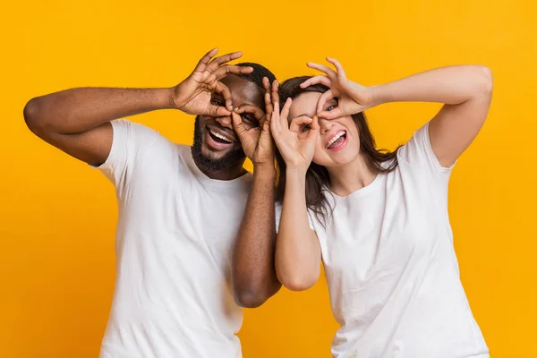 Alegre interracial casal fazendo engraçado óculos com dedos, enganando juntos — Fotografia de Stock