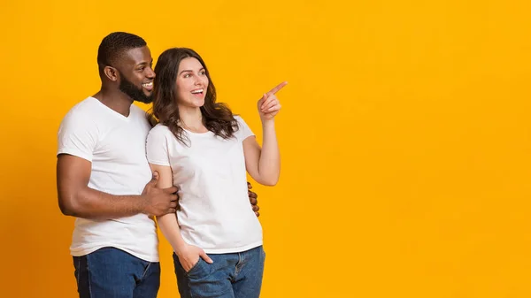 Happy interracial spouses cuddling and pointing aside at copy space — Stock Photo, Image