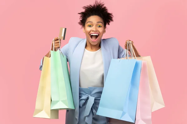 Chica afro alegre sosteniendo bolsas de compras y tarjeta de plástico —  Fotos de Stock