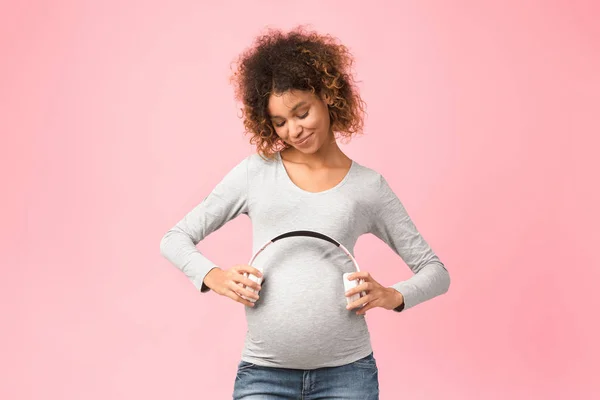 Graviditet och musik. Afro förväntansfull kvinna som håller hörlurar nära magen — Stockfoto