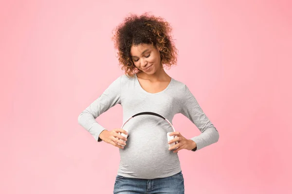 Gravidez e música. Afro mulher expectante segurando fones de ouvido perto da barriga — Fotografia de Stock