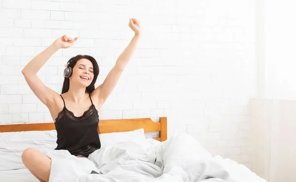 Беззаботная женщина слушает музыку, танцует в постели — стоковое фото