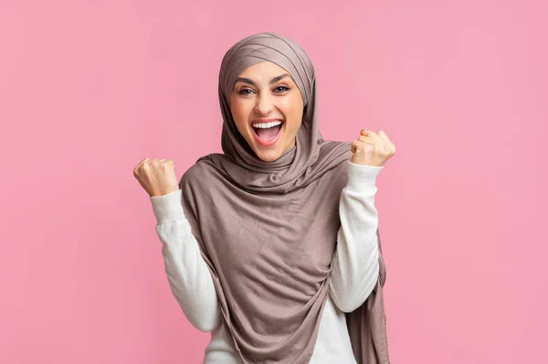 Überglückliches arabisches Mädchen mit Kopftuch feiert Erfolg vor rosa Hintergrund. — Stockfoto