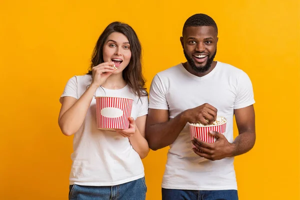 Alegre interracial casal comer pipoca, desfrutando cinema lanche sobre amarelo fundo — Fotografia de Stock