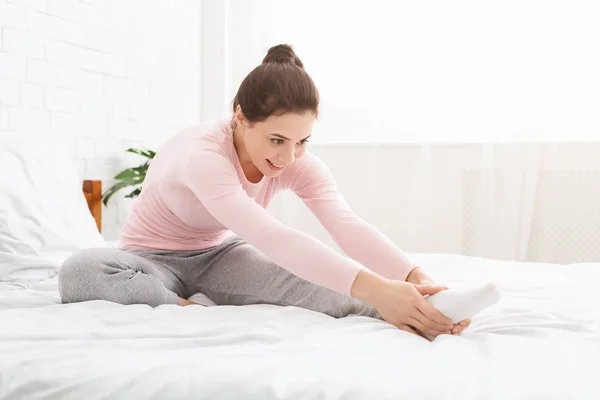 Jeune femme étirant ses jambes et faisant du yoga dans son lit — Photo