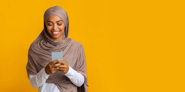 Alegre preto muçulmano menina no hijab com smartphone sobre fundo amarelo — Fotografia de Stock