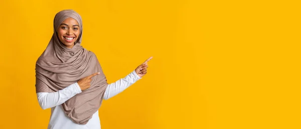 Smiling black muslim woman pointing at copy space on yellow background — Stock Photo, Image