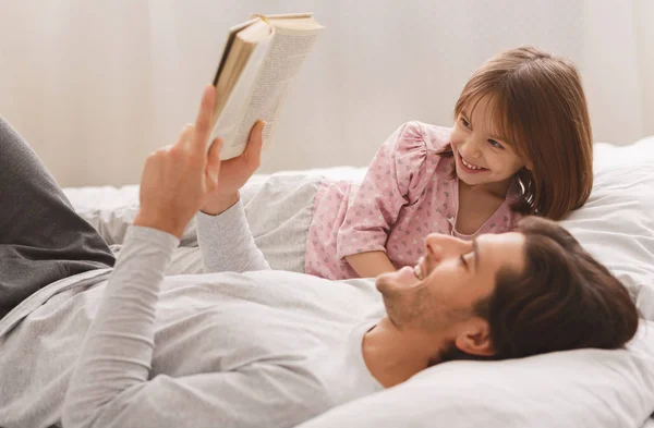 Jovem homem lendo livro para sua pequena filha sorridente — Fotografia de Stock