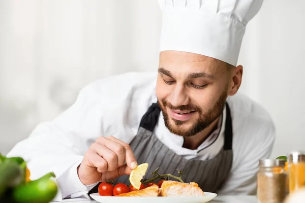 Profissional Chef Guy chapeamento prato de salmão de pé na cozinha do restaurante — Fotografia de Stock