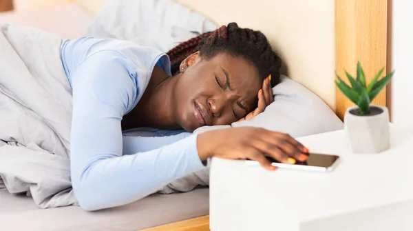 Mulher desligando alarme-relógio no telefone Heaving dor de cabeça na cama — Fotografia de Stock