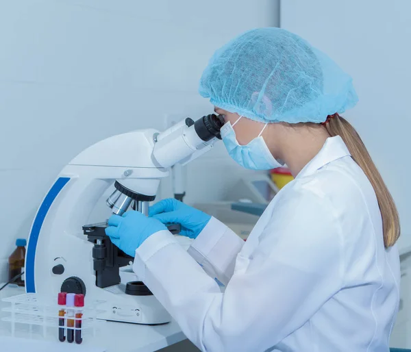 Девушка-лаборантка смотрит в объектив микроскопа — стоковое фото