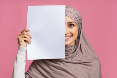 Yüzünün yarısını boş kağıtlarla örten gülümseyen Arap kız.