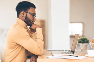 Evde dizüstü bilgisayarıyla çalışan siyah bir adam.