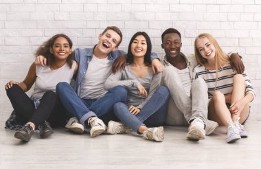 Öğrenciler beyaz tuğla duvarda sarılıp eğleniyorlar.
