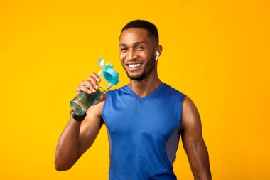 Siyah sporcu elinde su şişesiyle müzik dinliyor.