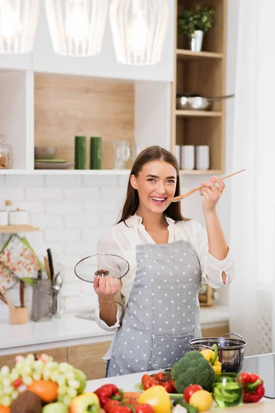 Happy woman in apron holding wooden spoon and smiling — Stock Photo, Image