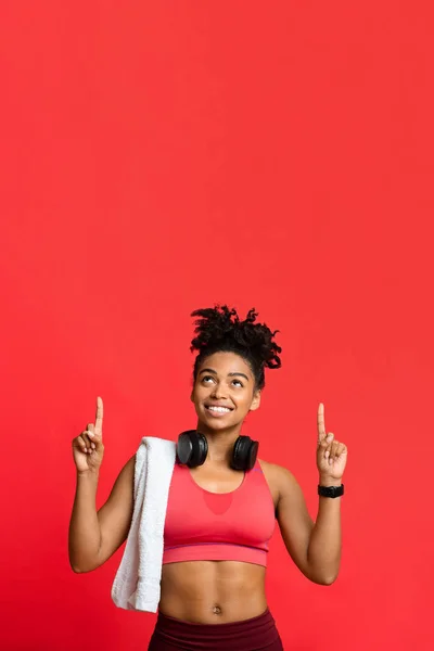 Glad afro sportig flicka med handduk och hörlurar pekar upp — Stockfoto