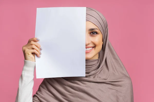 Sonriente chica árabe cubriendo la mitad de la cara con hoja de papel en blanco — Foto de Stock