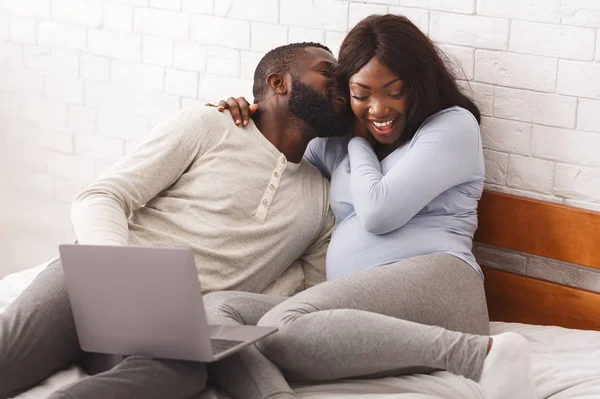 Schwangere und ihr Mann liegen mit Laptop im Bett — Stockfoto