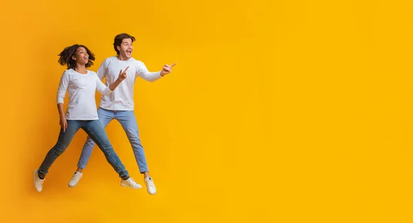 Casal interracial pulando no ar e apontando para o espaço de cópia — Fotografia de Stock