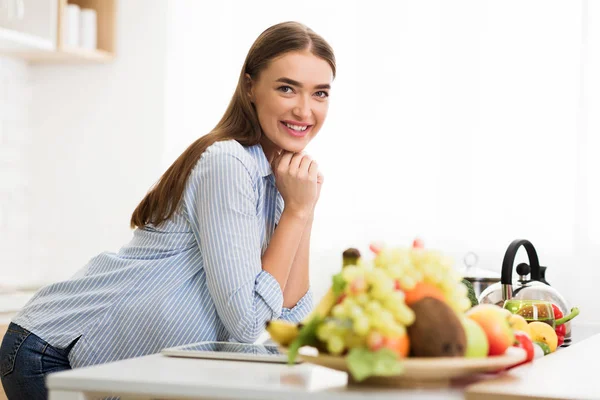 Kvinna poserar i kök nära bord med färska frukter — Stockfoto