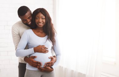 Neşeli hamile aile, pencerenin yanında poz veriyor.