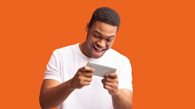 Turuncu arka planda cep telefonu kullanan heyecanlı afro adam.