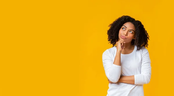 Menina afro duvidosa pensando em algo sobre fundo amarelo — Fotografia de Stock