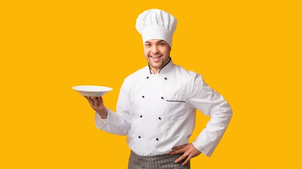 Chico cocinero sonriente sosteniendo la placa de pie sobre el fondo amarillo, Panorama — Foto de Stock