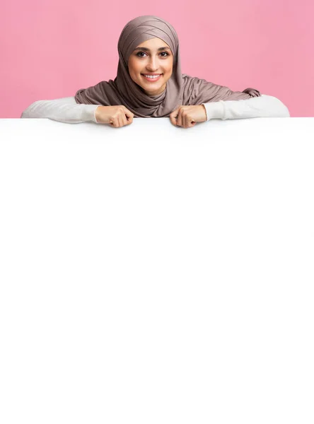 Smiling islamic girl in hijab leaning on white iklan board — Stok Foto