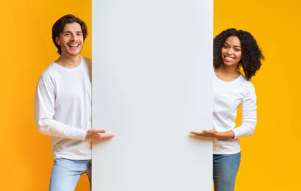 Fröhlicher Kerl und Afro-Girl zeigen auf weiße Werbetafel — Stockfoto