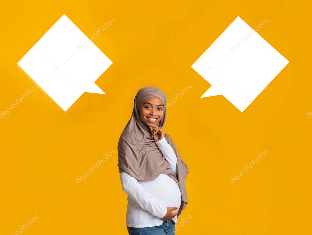 Pregnant afro muslim woman over background with two empty speech bubbles