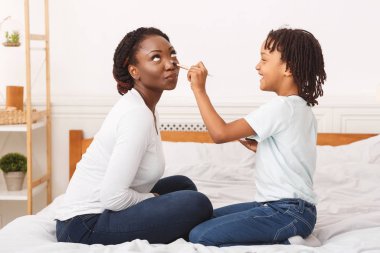Happy african child doing makeup for mommy