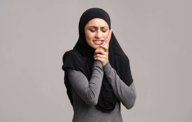 Sad muslim woman in hijab suffering from toothache, touching her cheek