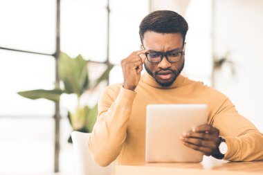 Surprised young afro manager looking at his tablet