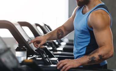 Athlete turning on modern treadmill at gym, panorama