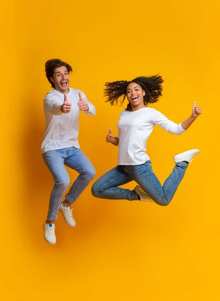Excited Multiracial Couple Jumping And Gesturing Thumbs Up, Having Fun Together — 스톡 사진