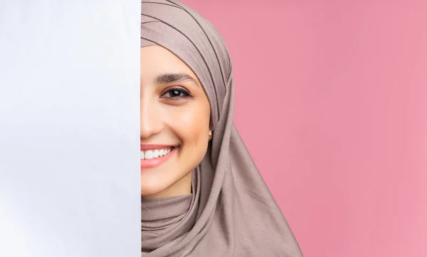 Lächelndes arabisches Mädchen, das hinter einer leeren Werbetafel steht und das halbe Gesicht verdeckt — Stockfoto