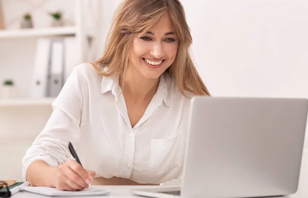 Empresária tomando notas trabalhando no laptop sentado no local de trabalho . — Fotografia de Stock