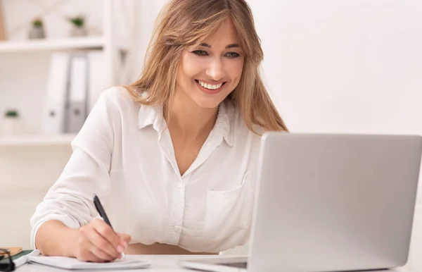 Zakenvrouw neemt notities werkend op laptop zittend op het werk. — Stockfoto