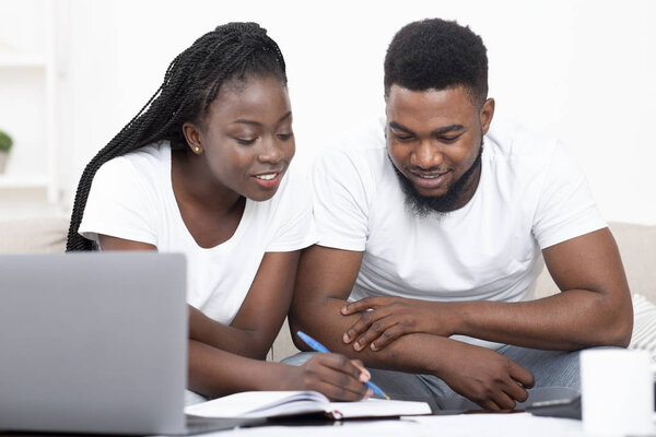 Молодая черная пара планируют бюджет вместе дома и писать заметки
