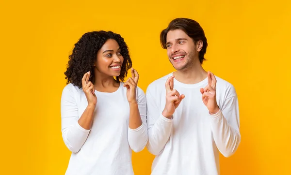 Feliz casal interracial cruzando dedos, implorando por algo — Fotografia de Stock