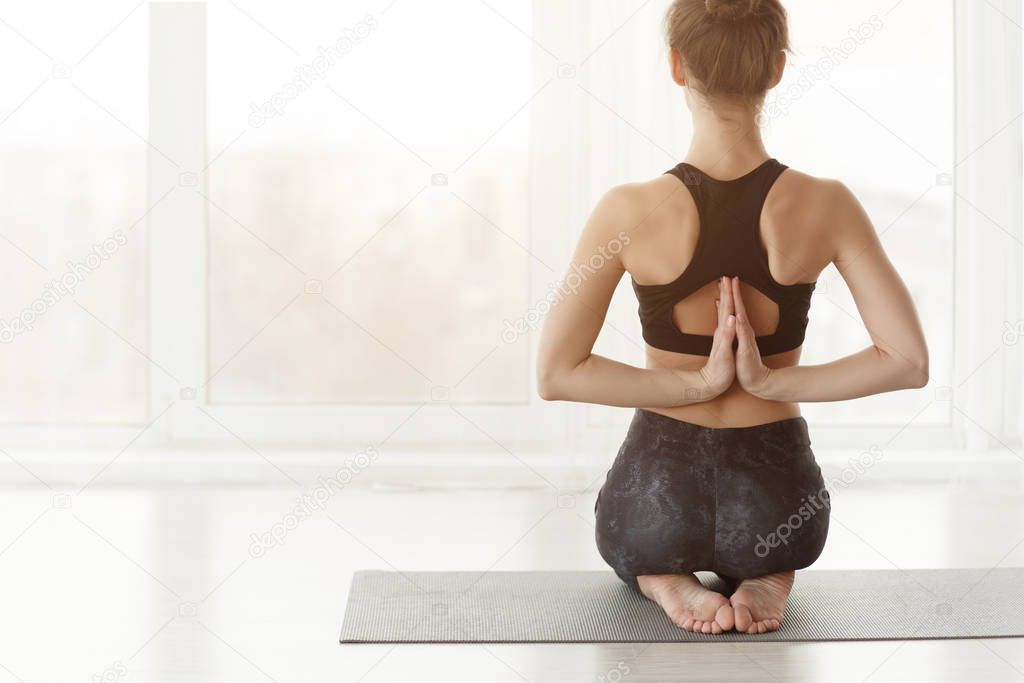 Woman sitting in Vajrasana pose with Namaste behind the back