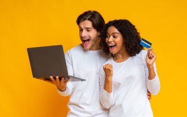 Joyful interracial couple rejoicing success with credit card and laptop