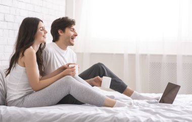 Happy spouses watching video on laptop and laughing in bed