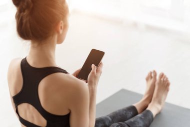 Girl using phone after practicing yoga on mat